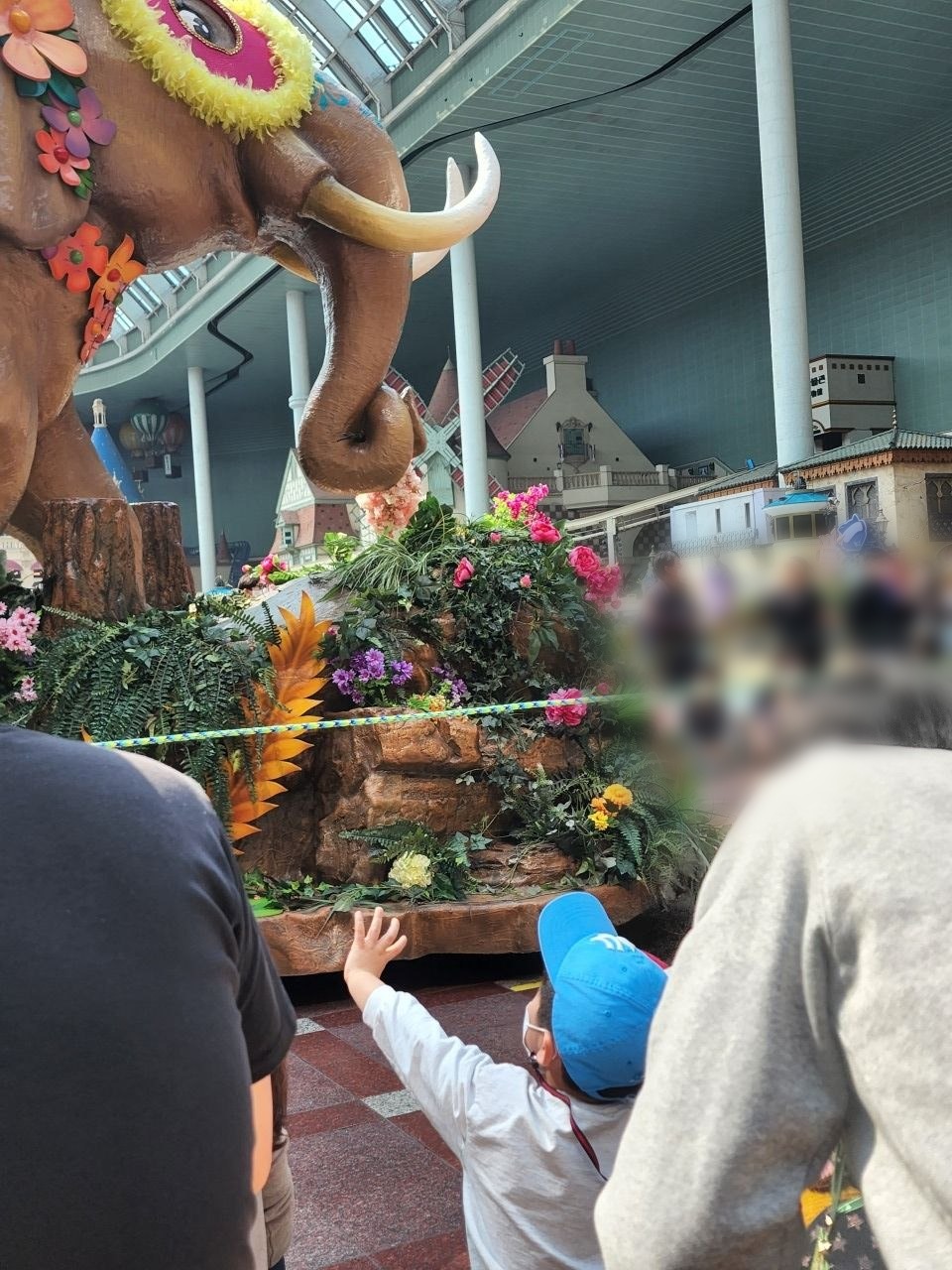 롯데월드 어드벤처 실내 광장에서 꽃으로 장식한 코끼리 퍼레이드 수레를 아이가 손을 흔들며 바라보는 모습