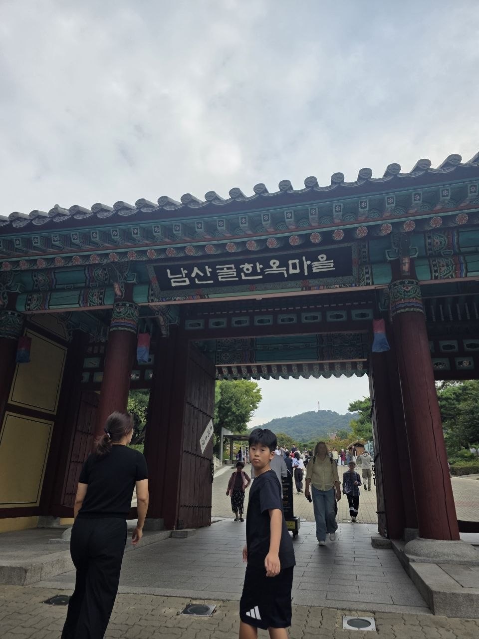 남산골한옥마을 정문, 단청이 칠해진 대문 위 남산골한옥마을 현판 아래로 가족이 들어서는 모습