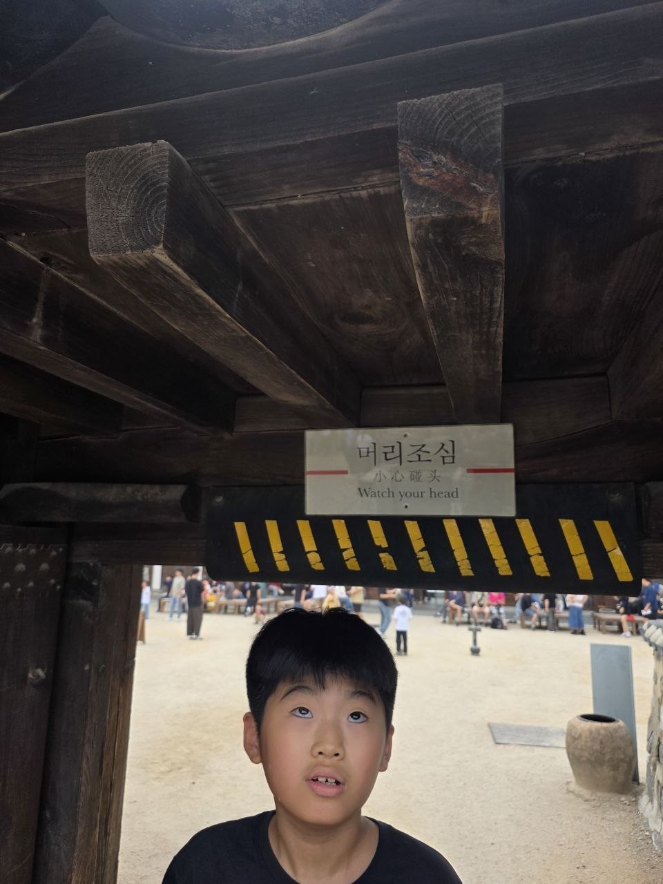 남산골한옥마을 한옥 문 아래 머리조심 표지와 노란 줄무늬 보 아래에서 아이가 위를 올려다보는 모습
