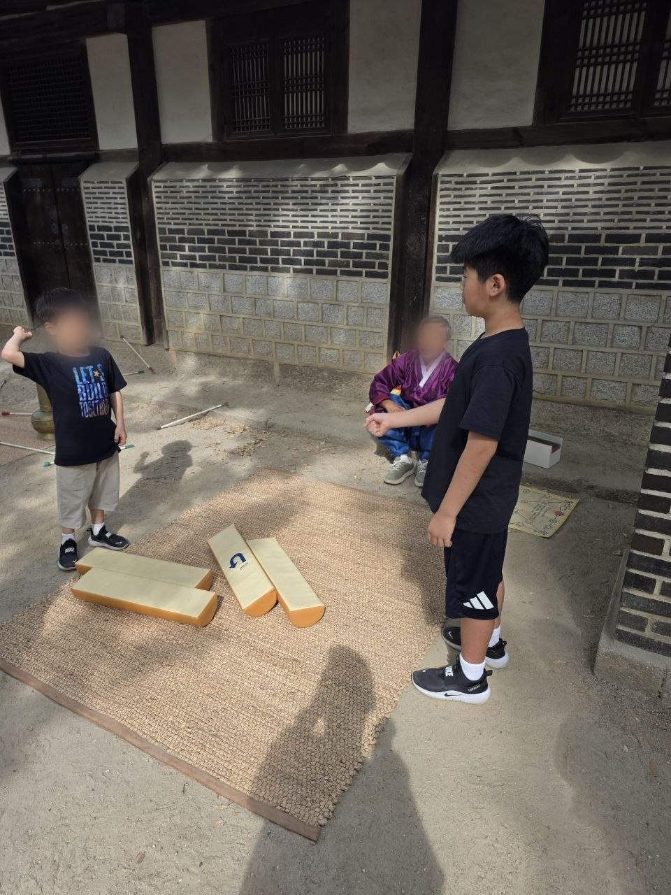 운현궁 담장 앞 멍석 위에 커다란 나무 윷 네 개가 놓여 있고 한복 입은 진행자 옆에서 아이 두 명이 윷을 던질 차례를 기다리는 모습