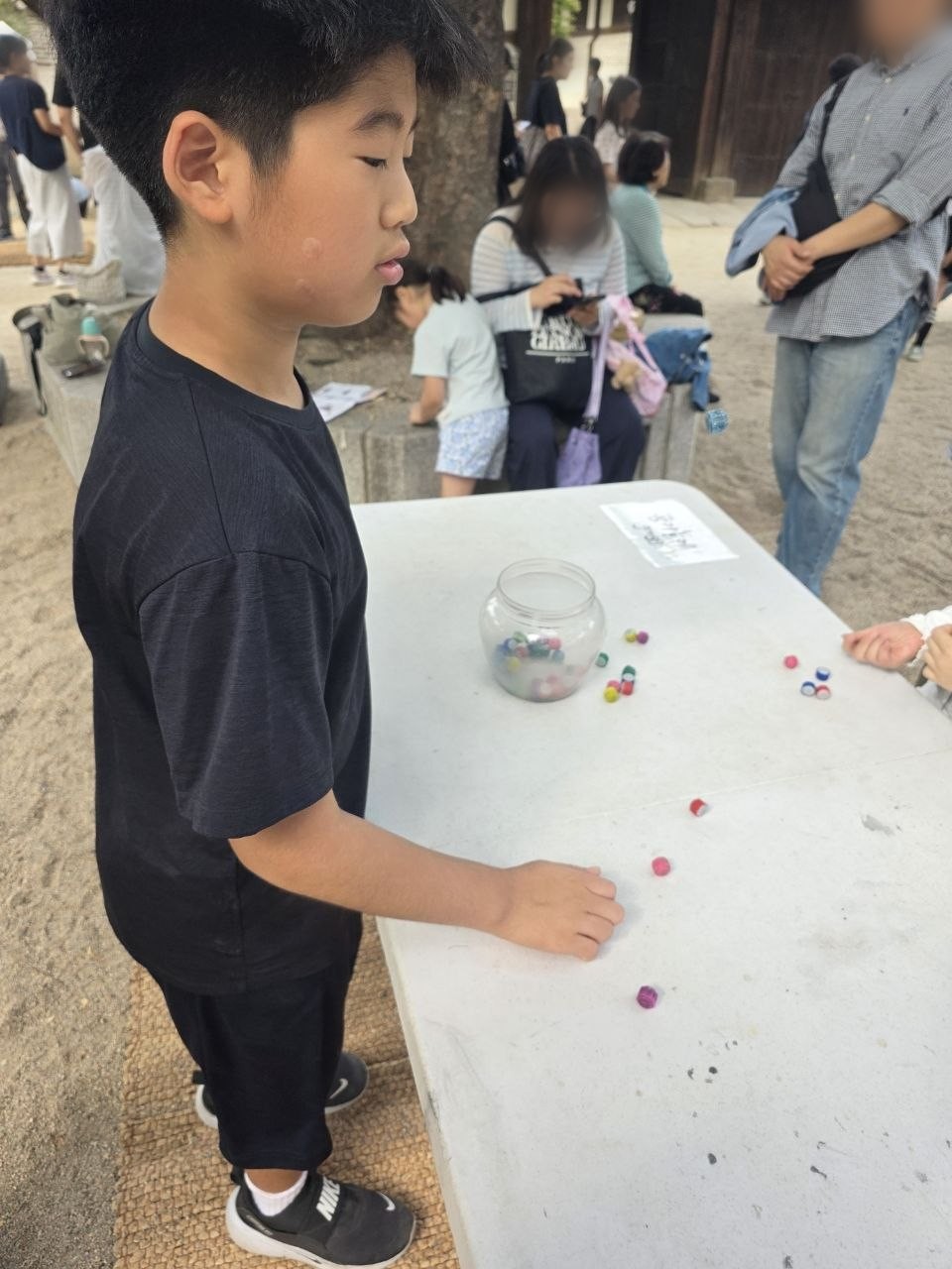 운현궁 마당 흰 탁자 위에 알록달록한 공깃돌이 흩어져 있고 아이가 탁자 앞에 서서 공기놀이를 하는 모습